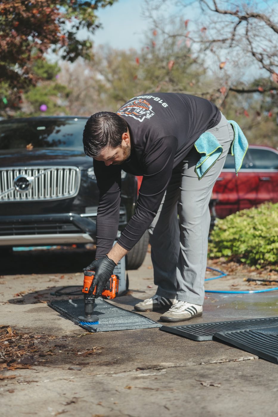 Scrubbing car floor mats with a drill brush on a driveway in the Tulsa metro