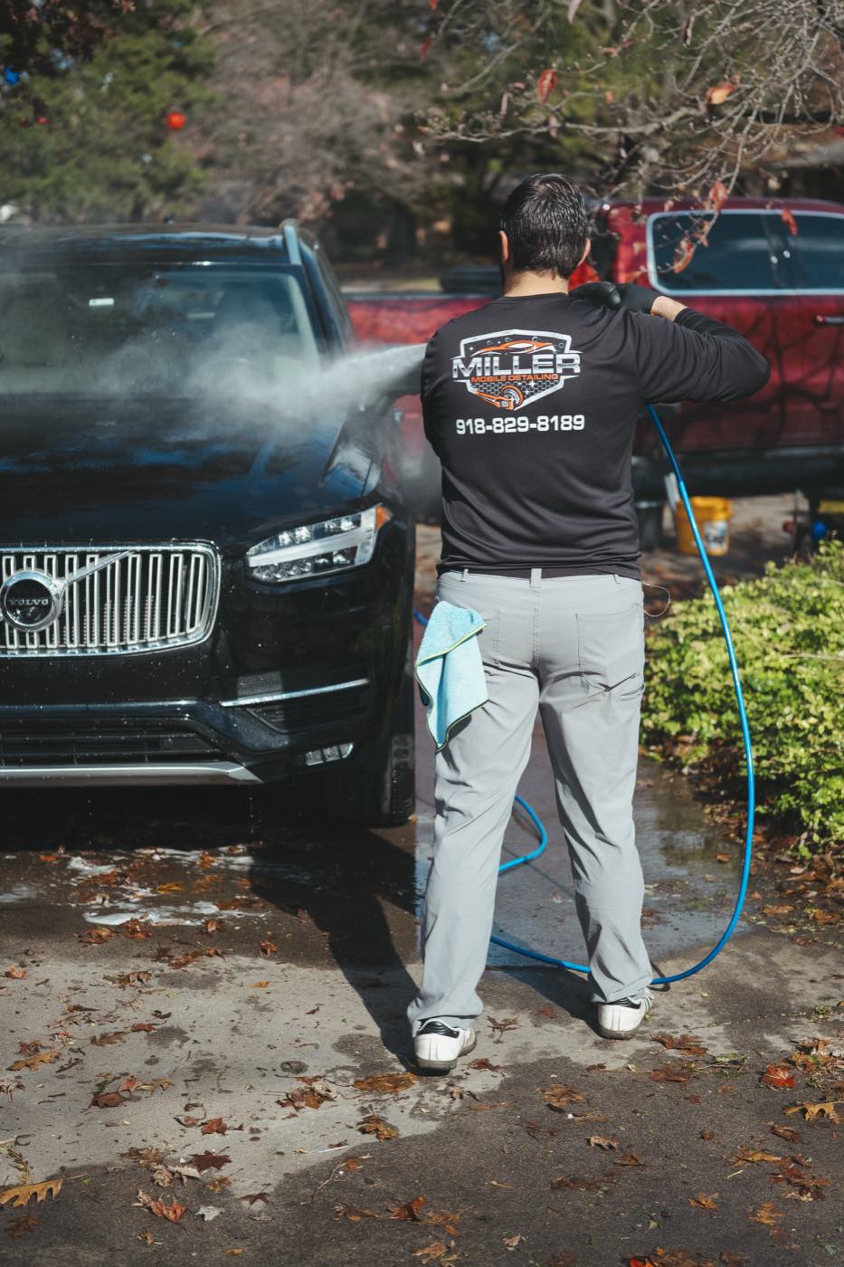Alex Miller of Miller Mobile Detailing pressure rinsing the front of a black SUV in a Tulsa driveway