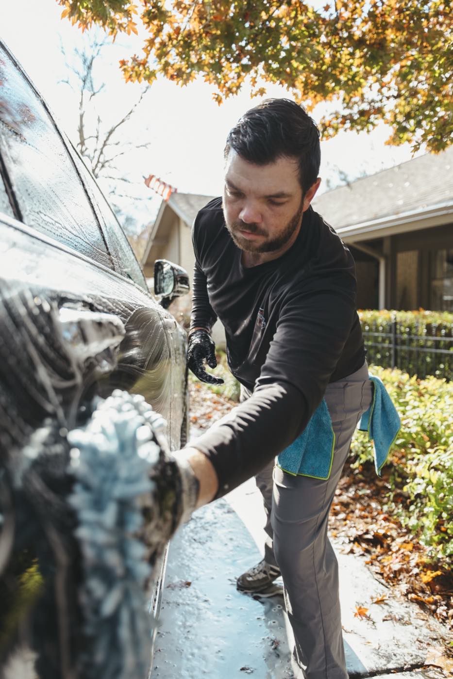 Hand washing a foamed SUV panel with a microfiber wash mitt at a customer's home in Tulsa